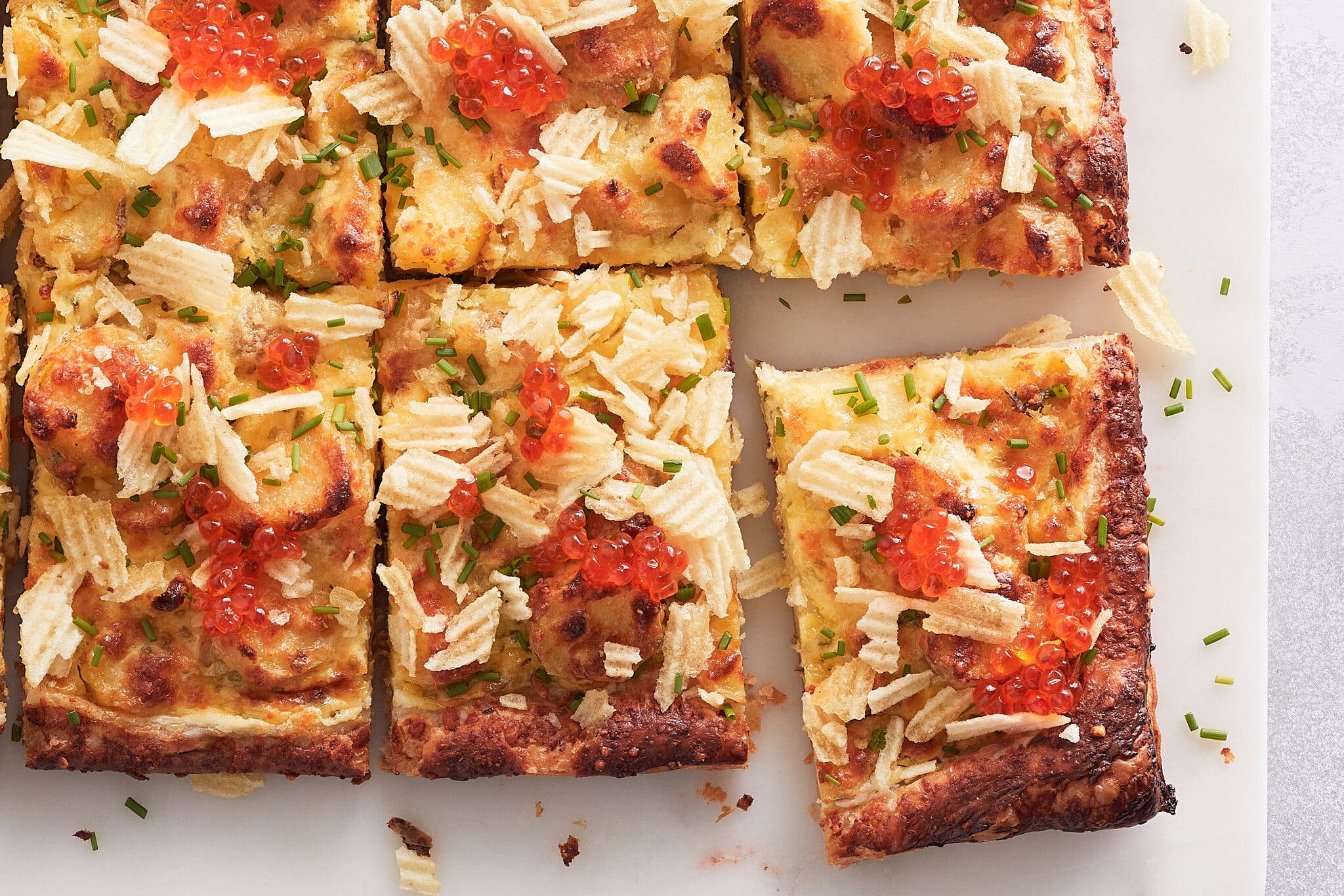 Six puff pastry rectangles topped with caviar and potato chips are photographed from overhead.