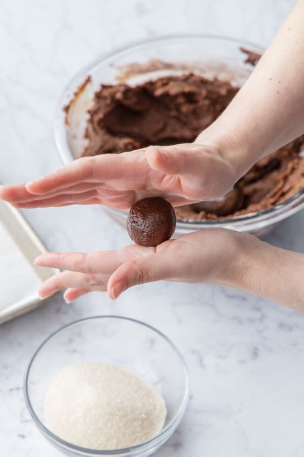 Rolling balls of cookie dough between hands to form a smooth ball.