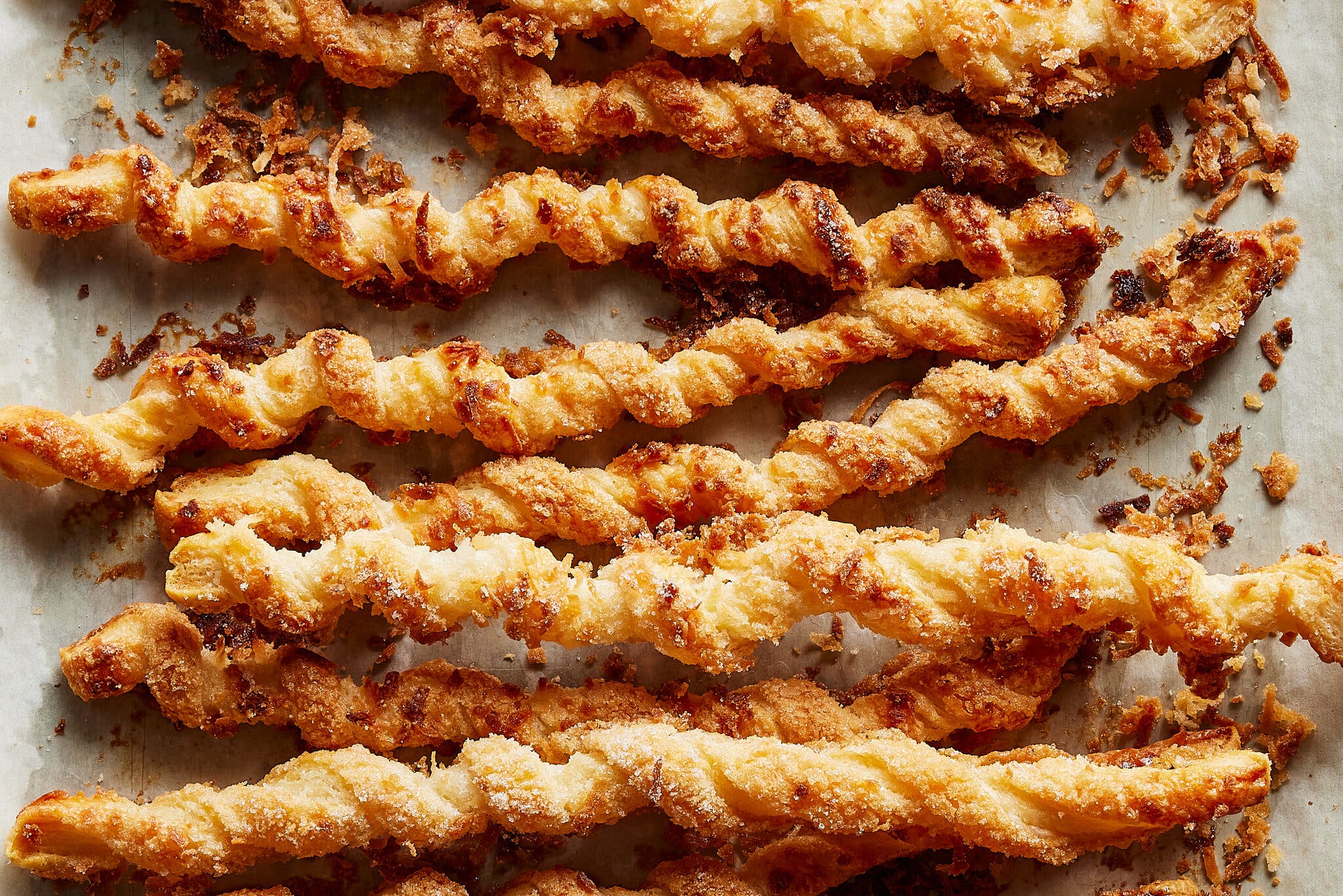 Twisted strands of puff pastry finished with crunchy sugar lay on parchment paper.