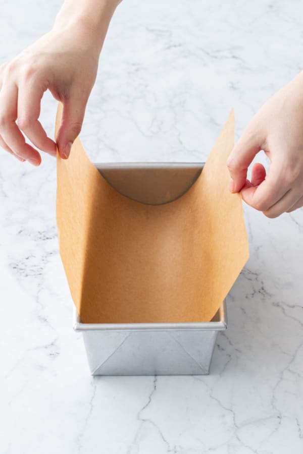 Lining a metal loaf pan with natural colored parchment paper.