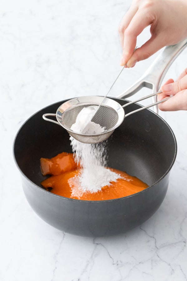 Sifting tapioca starch over persimmon puree in a saucepan.