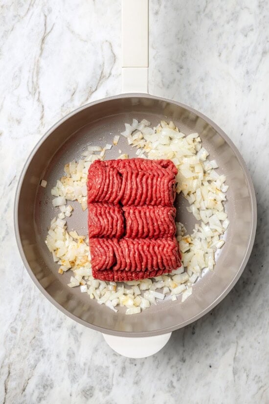 Overhead view of ground beef added to onions and garlic in skillet