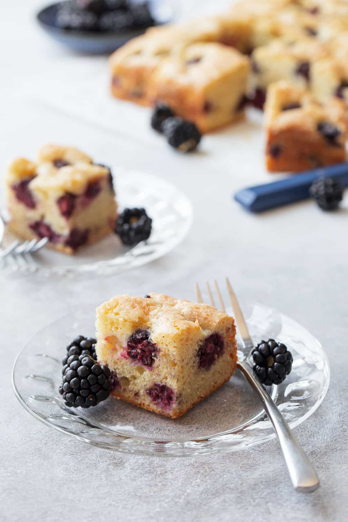 Cut squares of Blackberry Butter Cake on glass dessert plates, with silver fork and fresh blackberries.