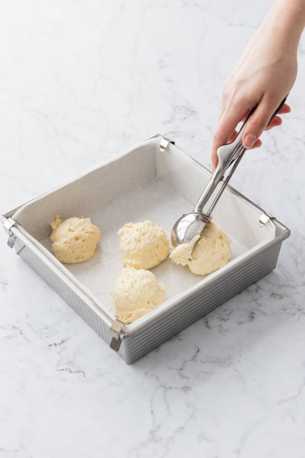 Using a large ice cream scoop to drop dollops of cake batter into a parchment-lined pan.