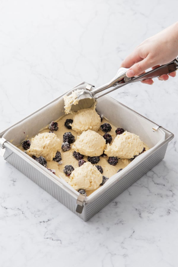 Scooping remaining cake batter into pan on top of first layer of cake and berries.