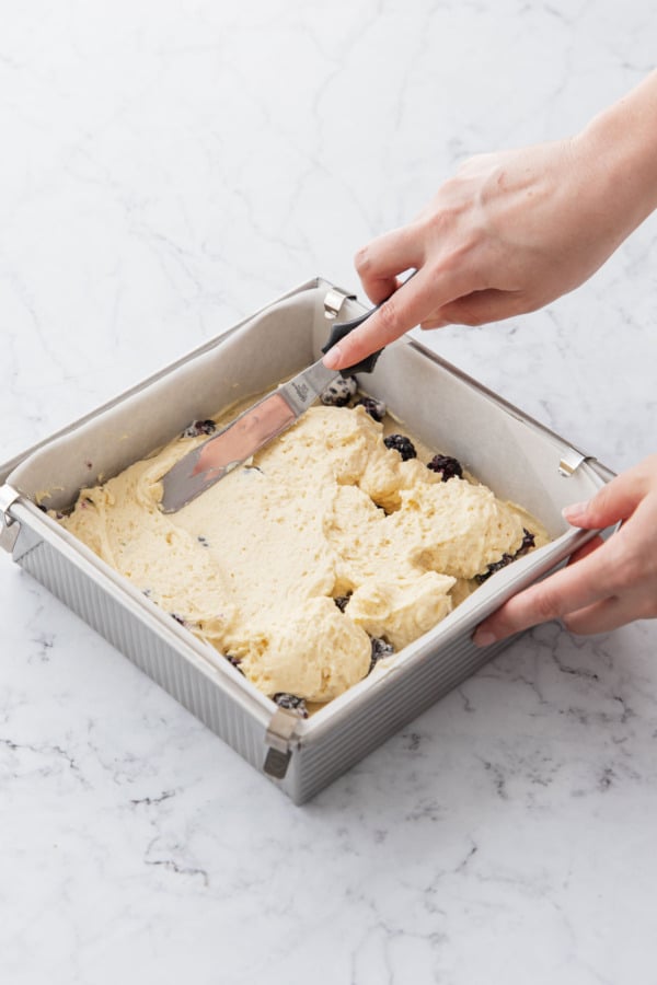 Spreading second layer of cake batter on top of berries using an offset spatula.