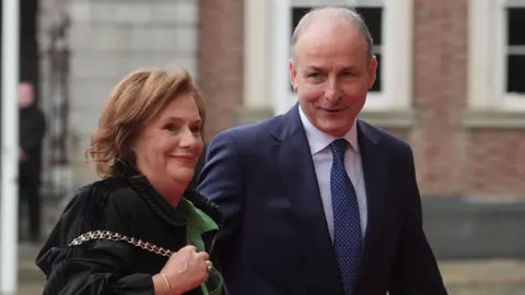 PA Media Mary O'Shea wearing a green and black coat, she has dark hair and Micheál Martin , he is wearing a navy suit with navy tie.