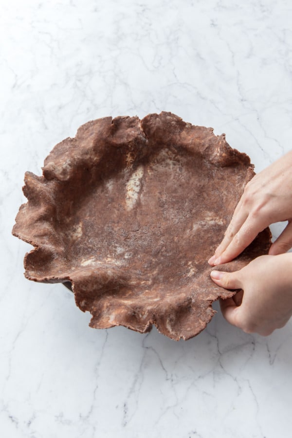 Unfolding the rolled pie dough and easing it into the corners of the pie pan.
