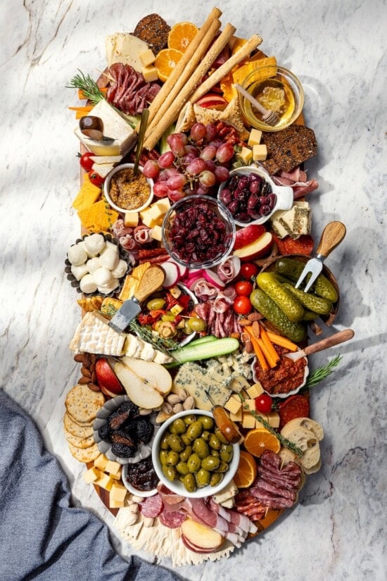Your ultimate guide to creating a charcuterie and cheese board! I'll show you how to choose and arrange everything for a beautiful spread. Large charcuterie and cheese board with fruit, pickles, olives, and spreads.