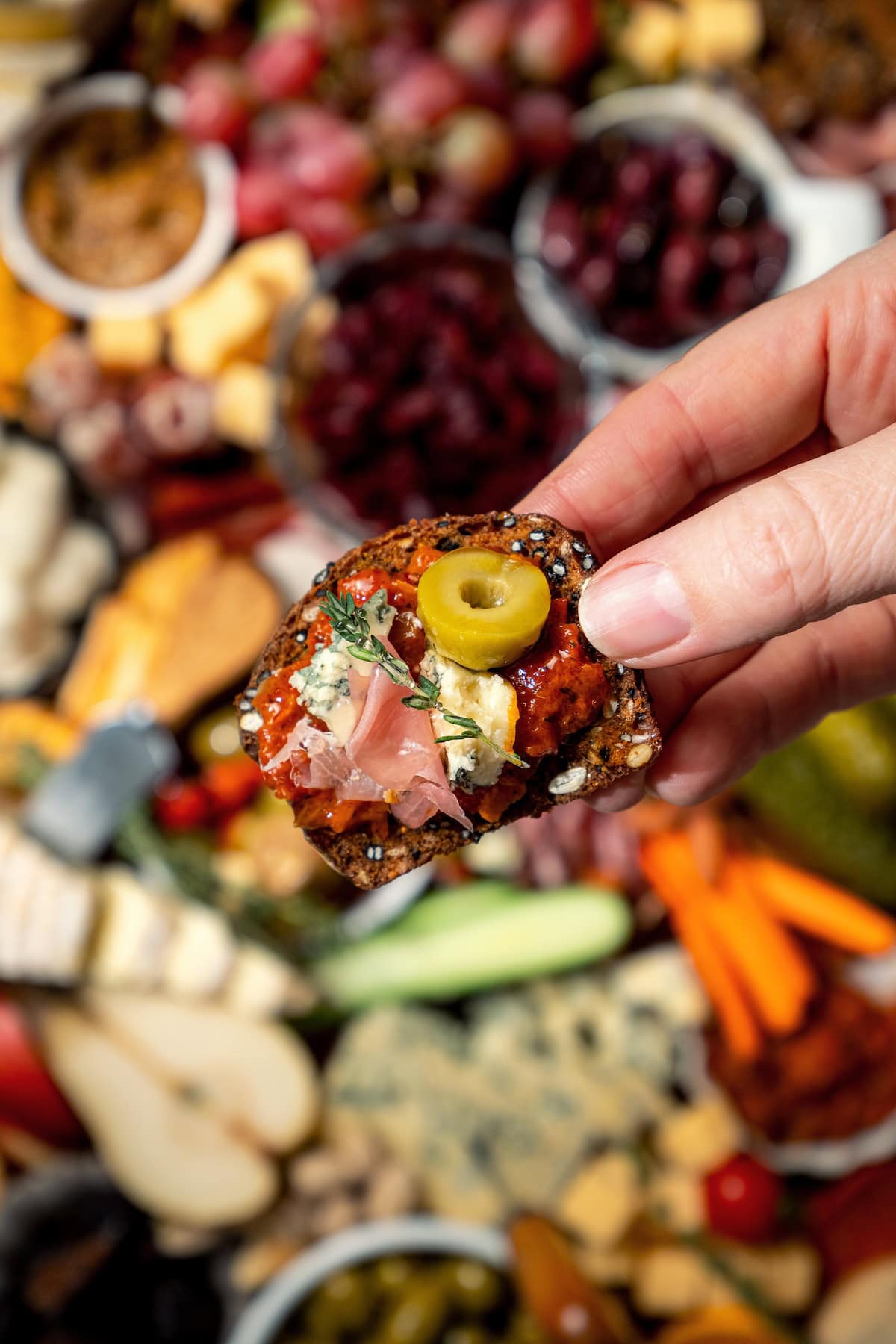 Your ultimate guide to creating a charcuterie and cheese board! I'll show you how to choose and arrange everything for a beautiful spread. Hand holding cracker topped with cheese, meat, and olive.